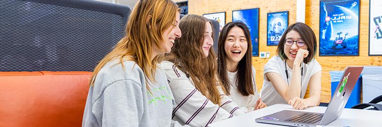 group of female students sitting down in front of a computer smiling and laughing