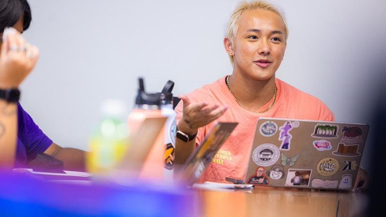 学生们在课堂上进行对话. There are water bottles and laptops with stickers on the desks.