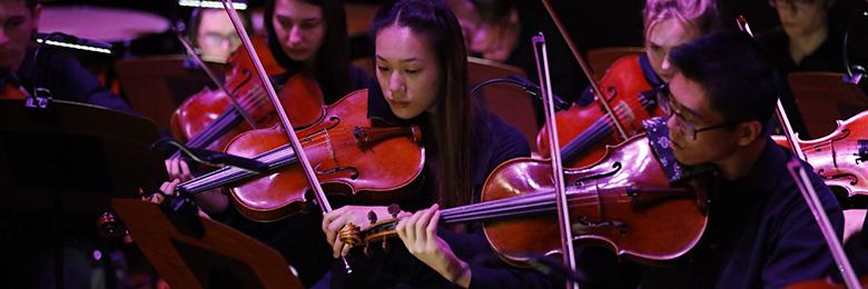 两名学生小提琴手在弱光下表演的特写.